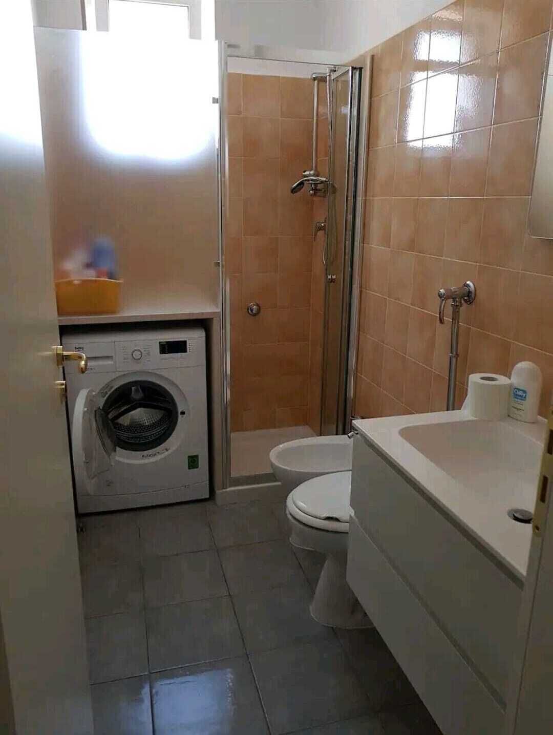 A compact bathroom with a washing machine, toilet, and shower.
