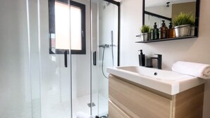 Ein modernes Badezimmer mit Duschkabine aus Glas, einem Holzwaschtisch mit Waschbecken und einem Spiegel darüber.