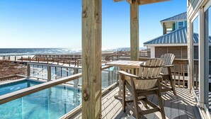 Une terrasse en bois avec une piscine, des chaises et une vue sur l’océan.