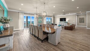 A spacious living room with a large dining table, wicker chairs, and a view through the glass doors.