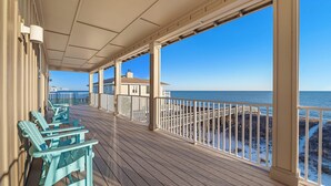 A covered deck with wooden flooring and white railings, overlooking a beach and ocean.