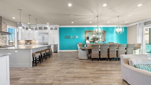 A modern kitchen with white cabinets, a central island with bar stools, and a dining area with wicker chairs.