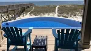 A pool with a wooden deck, two Adirondack chairs, and a view of the beach and ocean.