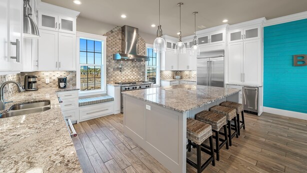 A modern kitchen with white cabinetry, a large island with bar stools, stainless steel appliances, and pendant lighting.