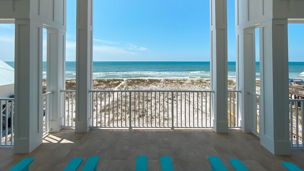 Blick auf einen Strand von einem überdachten Balkon mit weißen Geländern und hellem Boden.