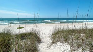 Ein Strand mit Sand und Gras im Vordergrund, der zum Meer führt.