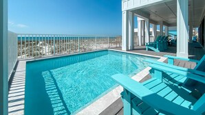 Ein Pool mit klarem, blauem Wasser, umgeben von einer weißen Liegefläche und blauen Liegestühlen.