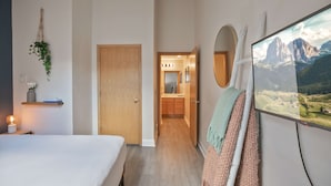 Ein Schlafzimmer mit einem Bett, einer Nachttischlampe, einer Wandpflanze und einem Fernseher, der eine Berglandschaft zeigt.