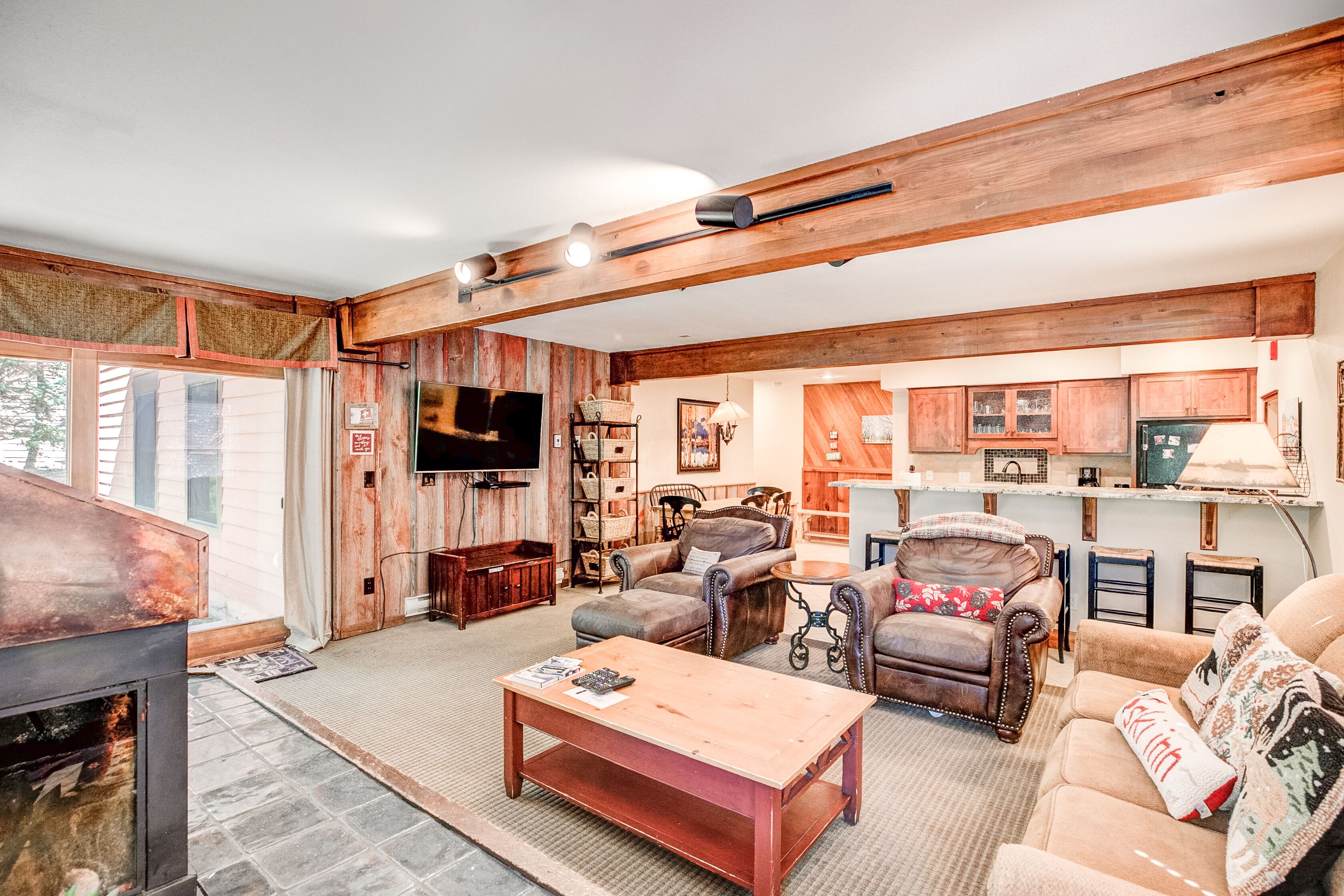 A cozy living room with a fireplace, leather sofas, a coffee table, and wooden beams on the ceiling.