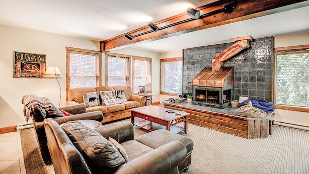 A cozy living room with a fireplace, leather sofas, and a wooden ceiling beam.