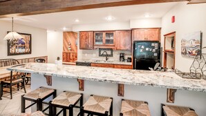 A modern kitchen with wooden cabinets, a marble countertop, and bar stools.