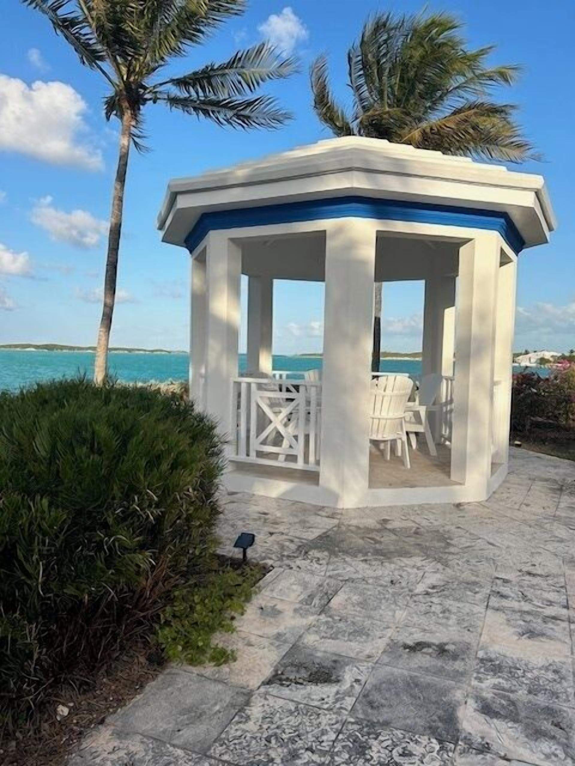 A gazebo with a view of the ocean, surrounded by palm trees and a stone pathway.