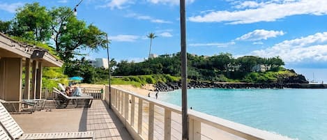 A wooden deck with lounge chairs, a railing, and a view of the sea.