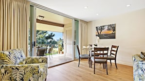 A spacious living area with a wooden floor, a dining table with chairs, and a sofa with a tropical print.