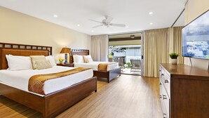 A hotel room with two beds, a ceiling fan, a TV, and a sliding glass door to the balcony.