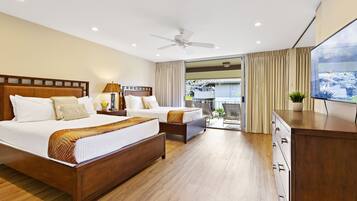 A hotel room with two beds, a ceiling fan, a TV, and a sliding glass door to the balcony.
