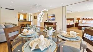 A dining area with round tables, chairs, and a central orchid. A kitchen and a bedroom are visible in the background.