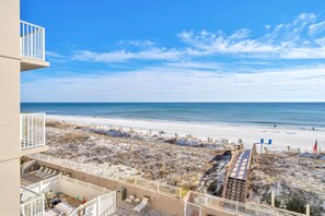 A beach view from a balcony with a sandy beach, a clear sky, and a few people in the distance.