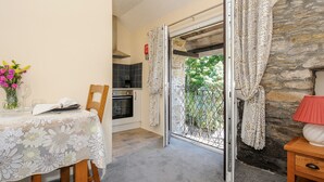 Un comedor acogedor con una mesa dispuesta para dos, un jarrón de flores y vistas a un muro de piedra y follaje.