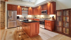 Une cuisine moderne avec des meubles en bois, des appareils en acier inoxydable et un îlot central doté de tabourets de bar.