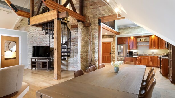 Une salle à manger spacieuse avec une longue table et des chaises en bois, une cheminée et un escalier menant à un niveau supérieur.