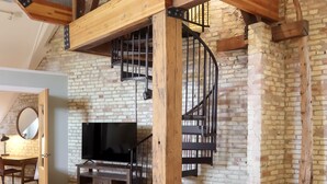 Un loft spacieux avec des poutres apparentes, un mur en briques et un escalier en colimaçon.