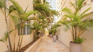 A narrow, paved corridor with potted palm trees and a building in the background. - OFP - Duplex na Oscar Freire By Anora Spaces (São Paulo)