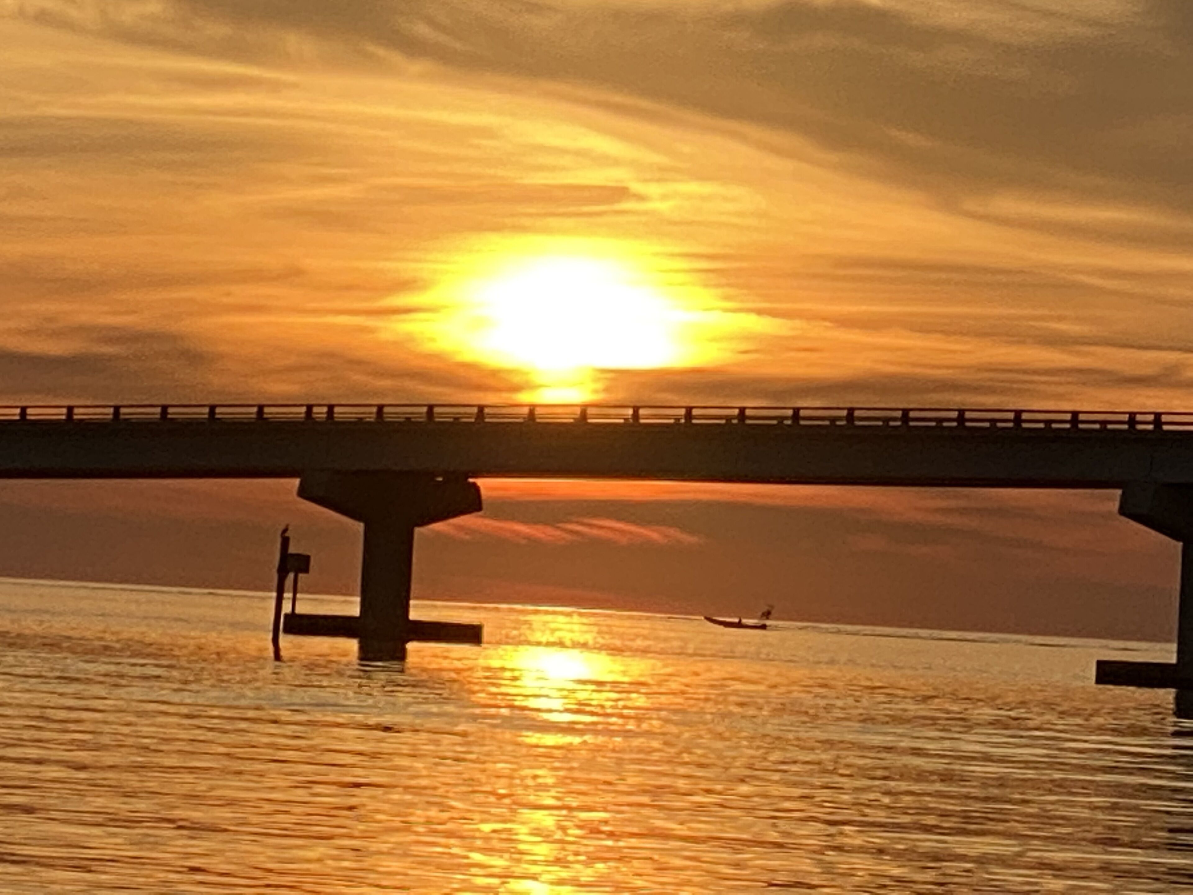 A sunset over a body of water with a bridge in the foreground.