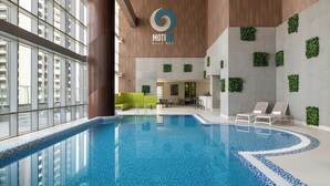 Una piscina interior con agua azul cristalina, rodeada por un interior moderno con techo de madera y jardineras colgantes de color verde.