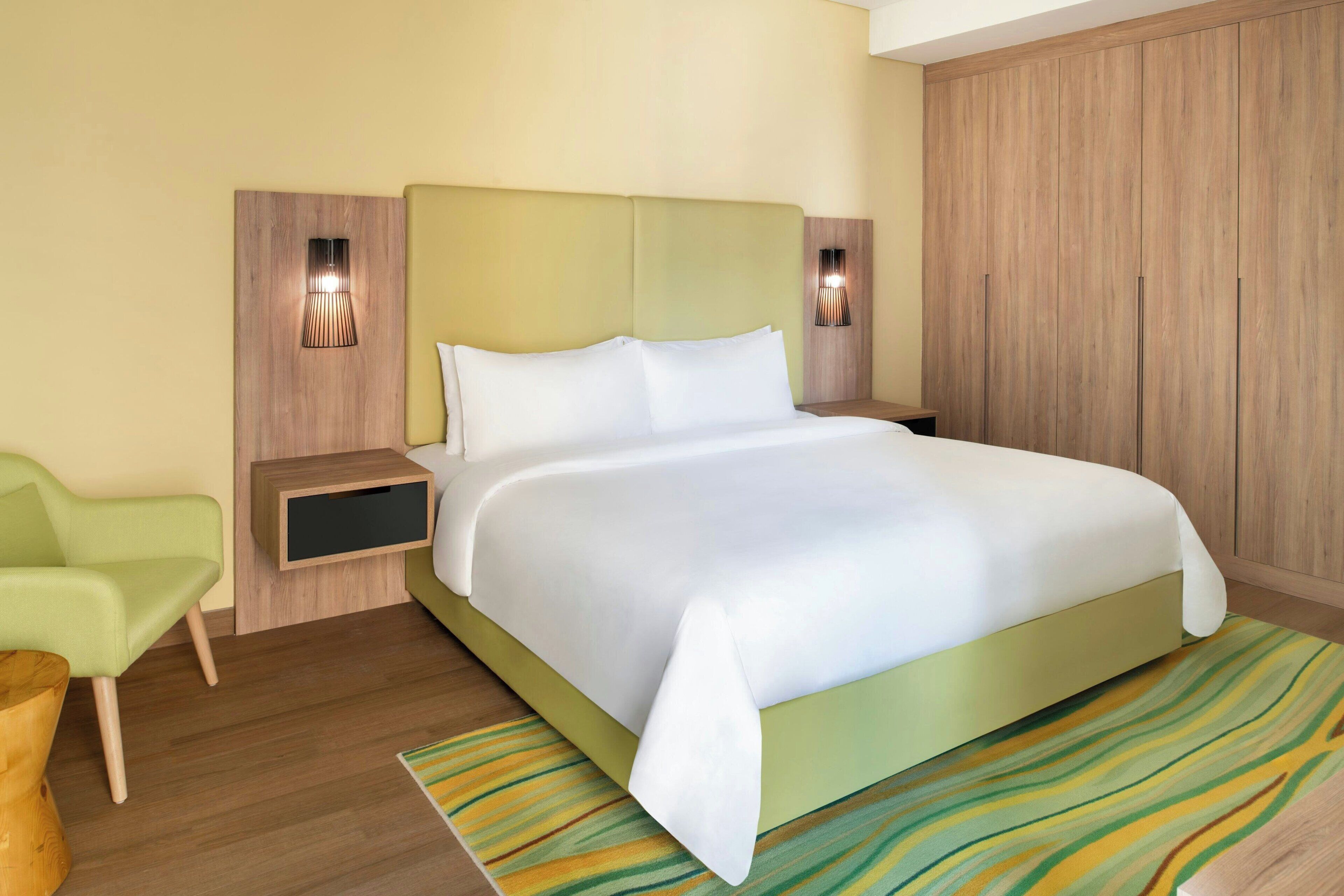 A modern hotel room with a large bed, a green accent wall, and two bedside lamps.
