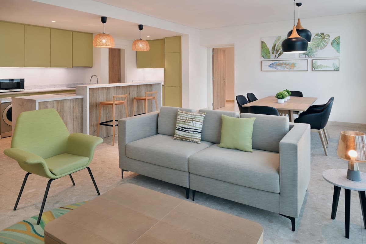 Una sala de estar moderna con un sofá gris, un sillón verde y un comedor con una mesa y sillas.