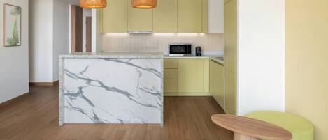 Una cocina moderna con una isla de mármol, armarios amarillos y una pared de acento verde.