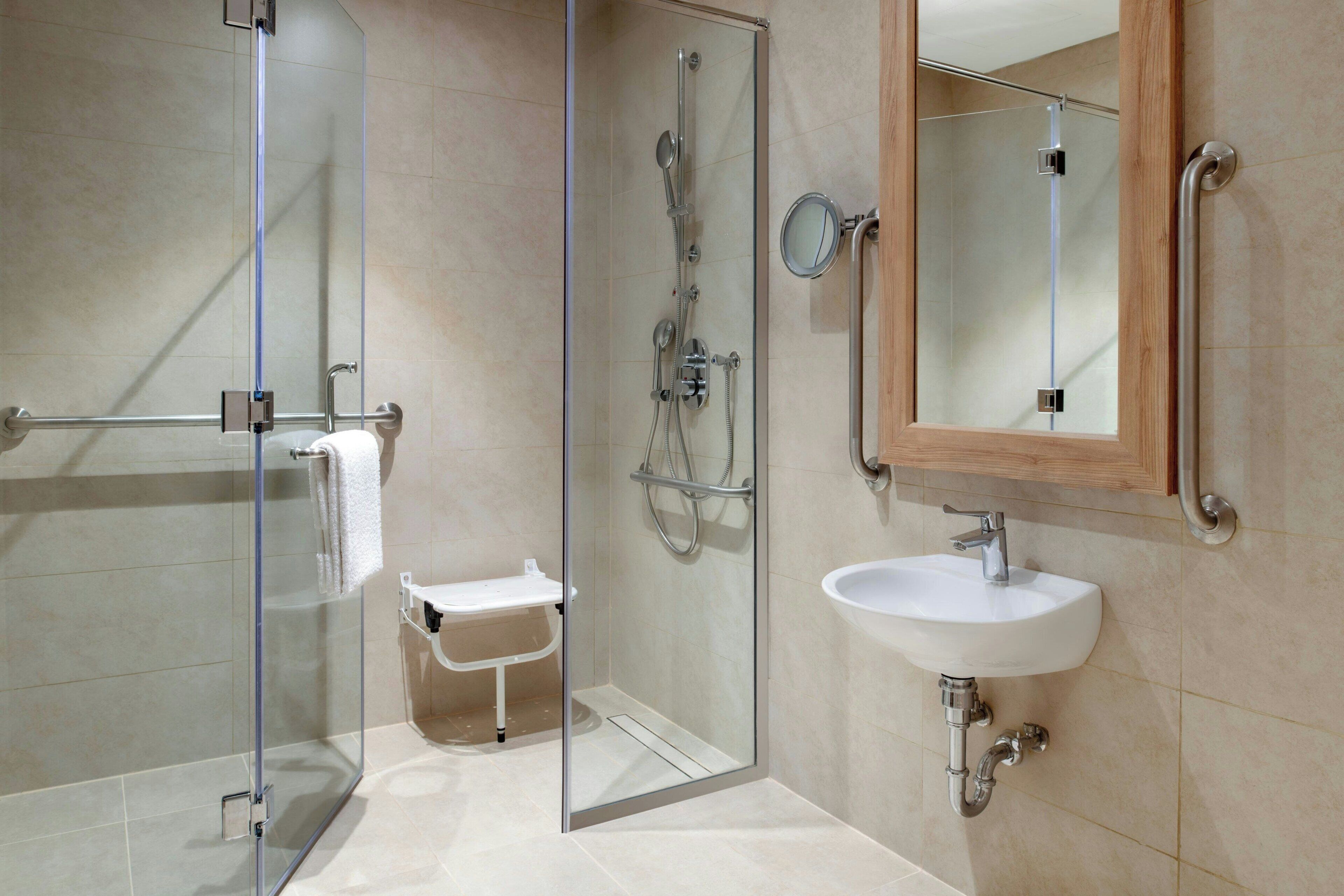 A modern bathroom with a glass-enclosed shower, a white sink, and a wooden-framed mirror.