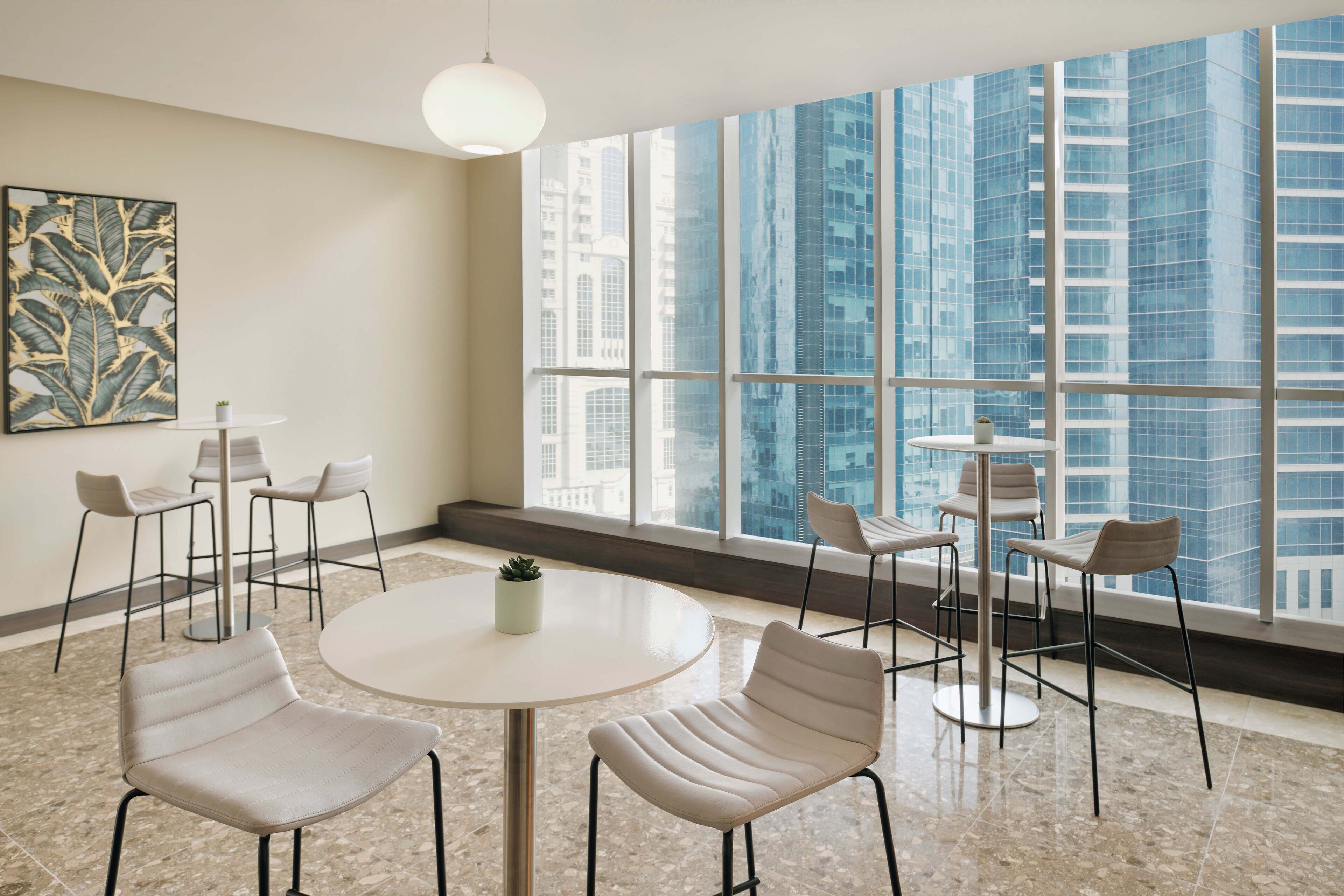 Een moderne vergaderruimte met een groot raam met uitzicht op hoge gebouwen. Er staan verschillende stoelen en een ronde tafel met een kleine plant.