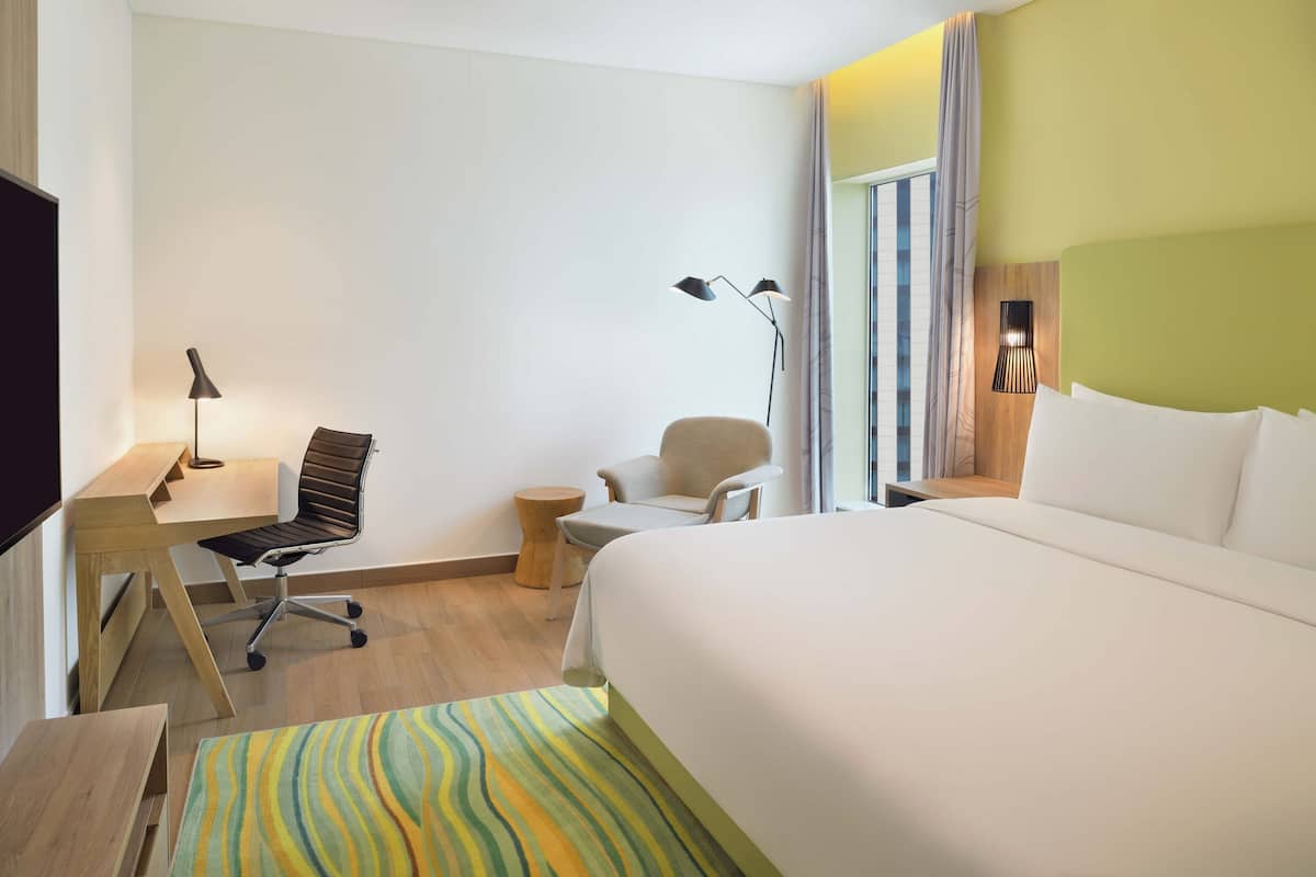 Habitación de hotel con una cama grande, un escritorio con silla, una mesita redonda y una lámpara.