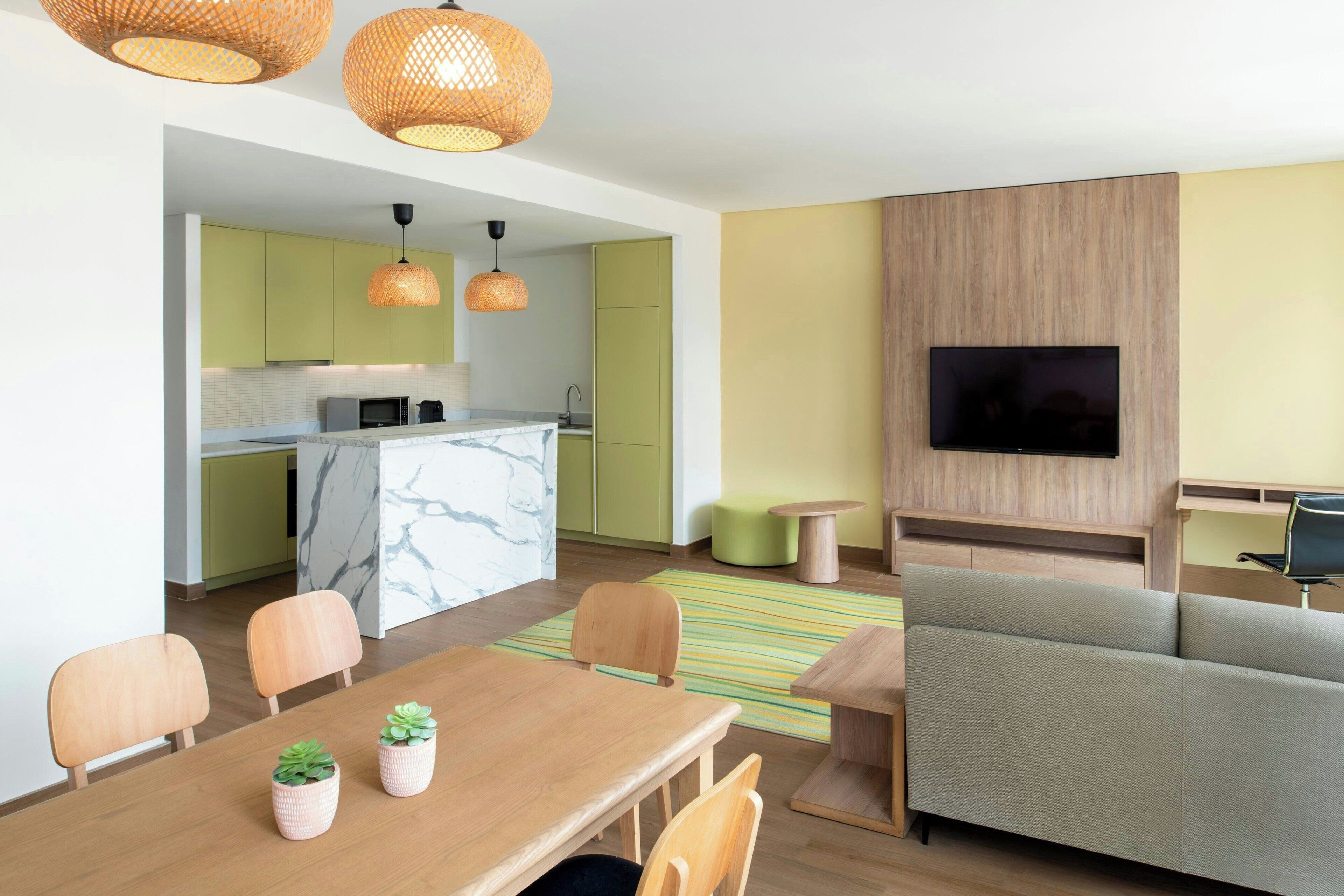 A modern living room with a sofa, a dining table with chairs, and a kitchen area with a TV.