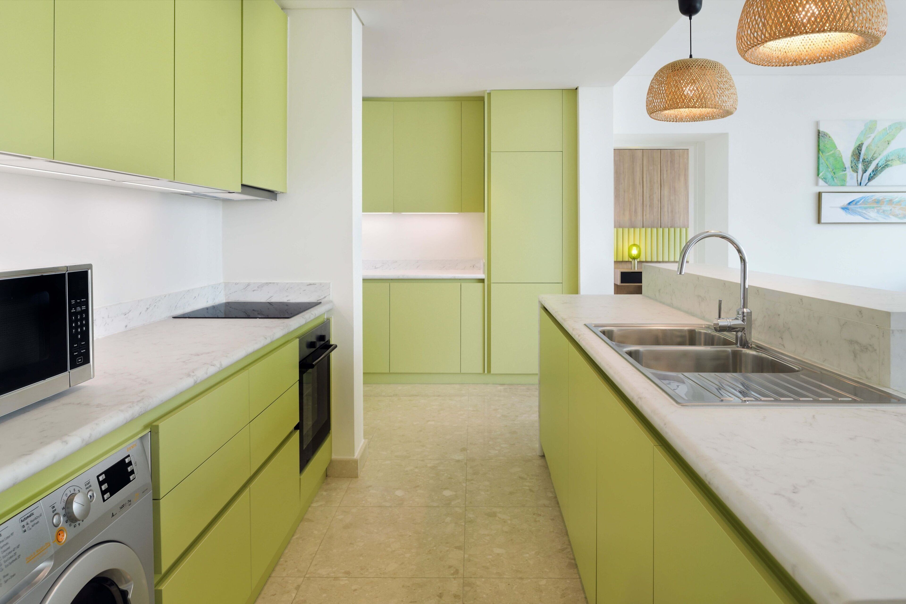 A compact kitchen with green cabinets, a built-in oven, a washing machine, a sink, and a microwave.