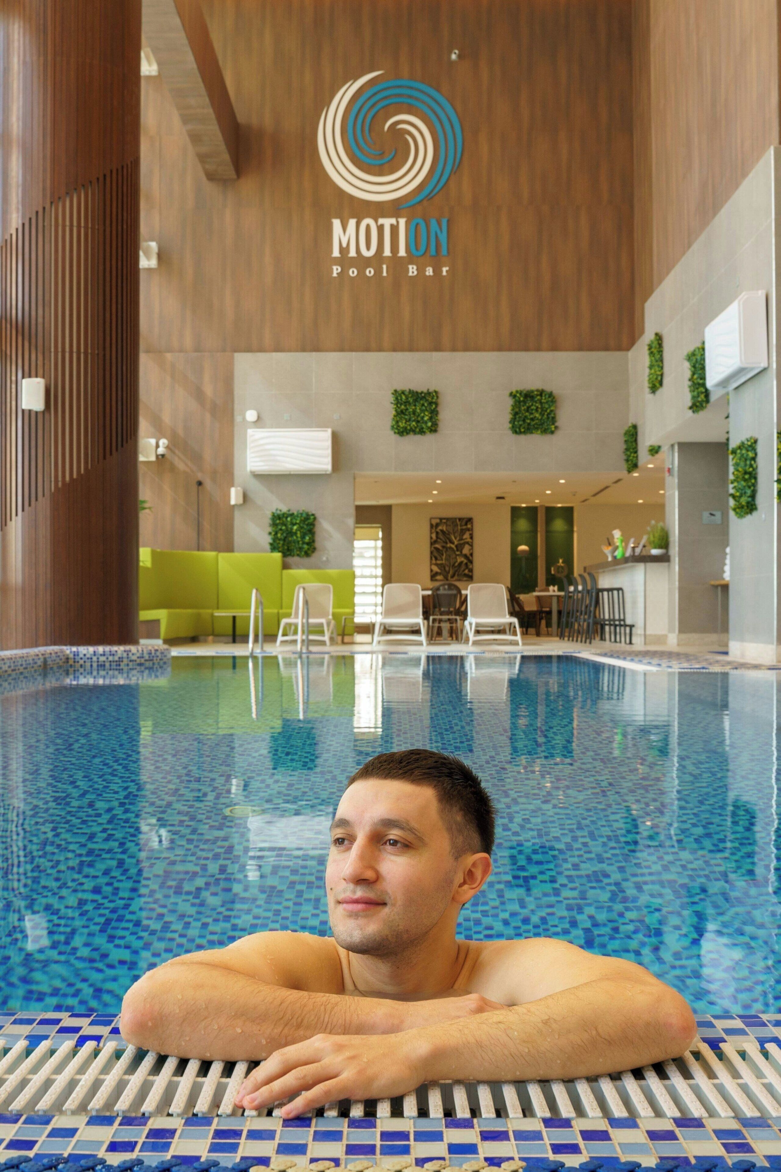 Um homem relaxando em uma piscina de hotel, com o logo 'MOTION Pool Bar' na parede.