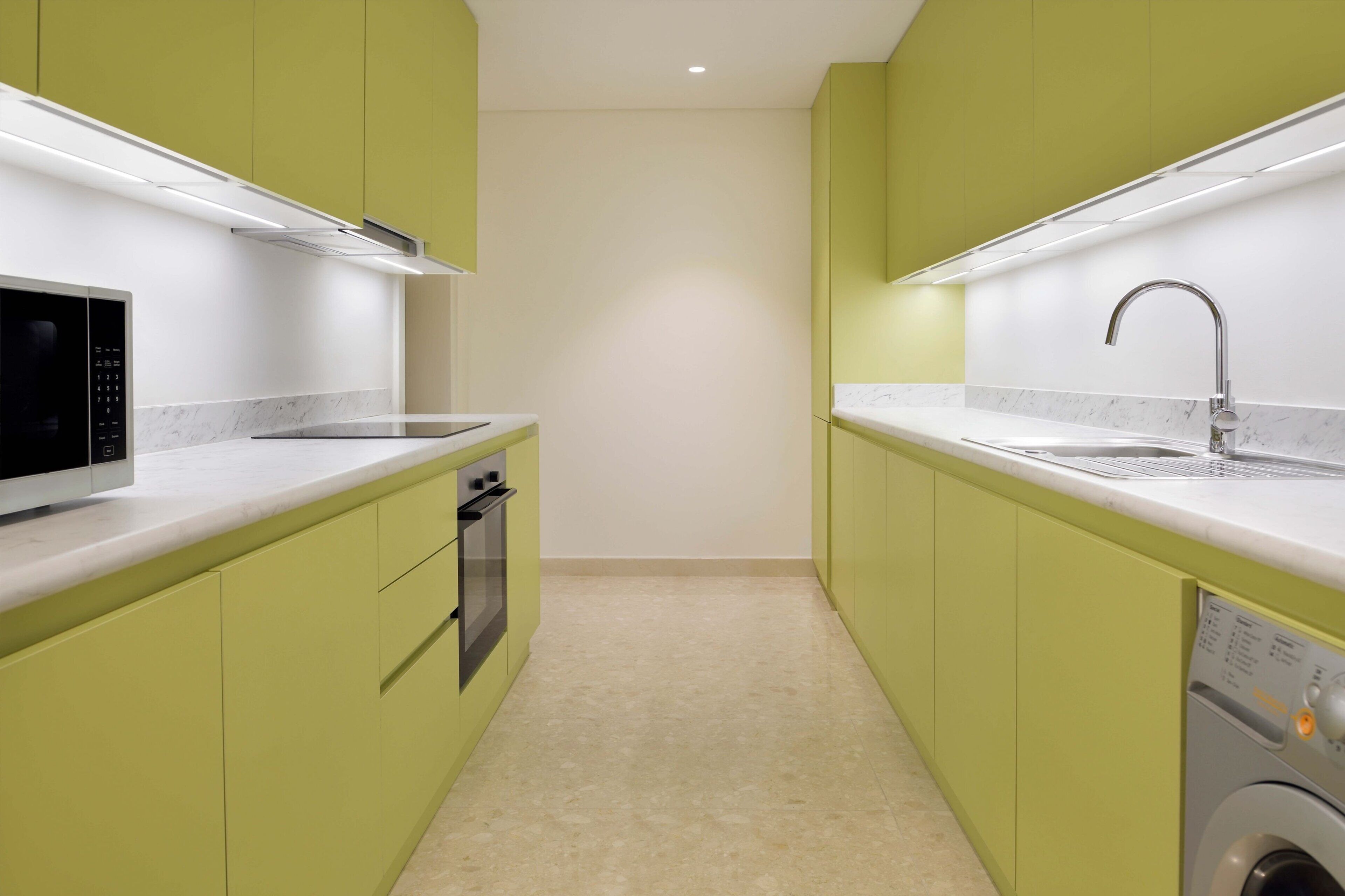 Cocina compacta con gabinetes verdes, microondas, horno, lavavajillas y lavadora.