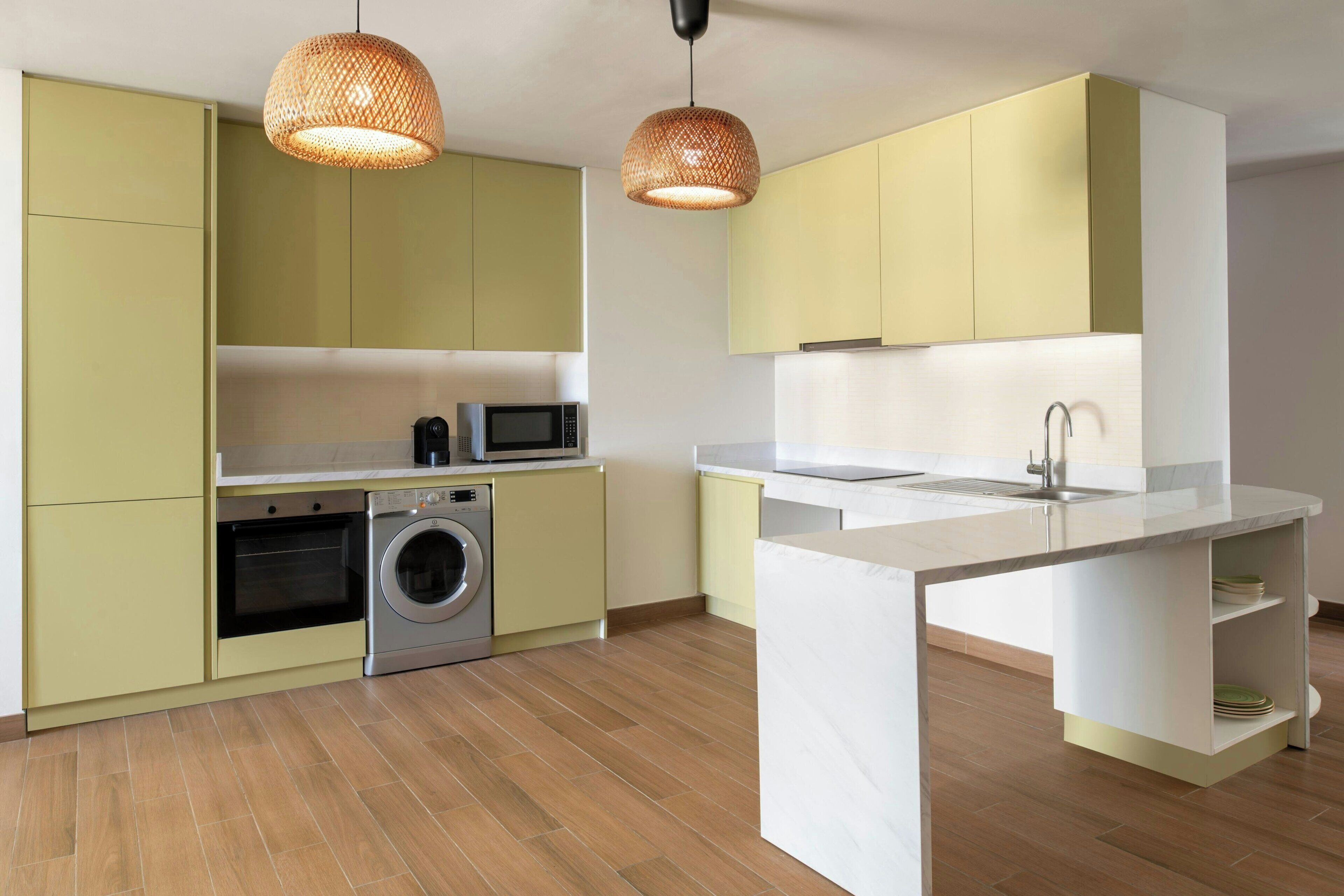 A modern kitchen with light green cabinets, a built-in washing machine, a microwave, and a white countertop island.