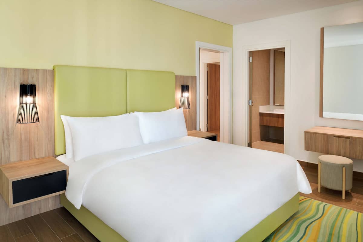 Habitación de hotel con una cama grande, mesitas de noche, un espejo y un baño a la vista a través de una puerta abierta.