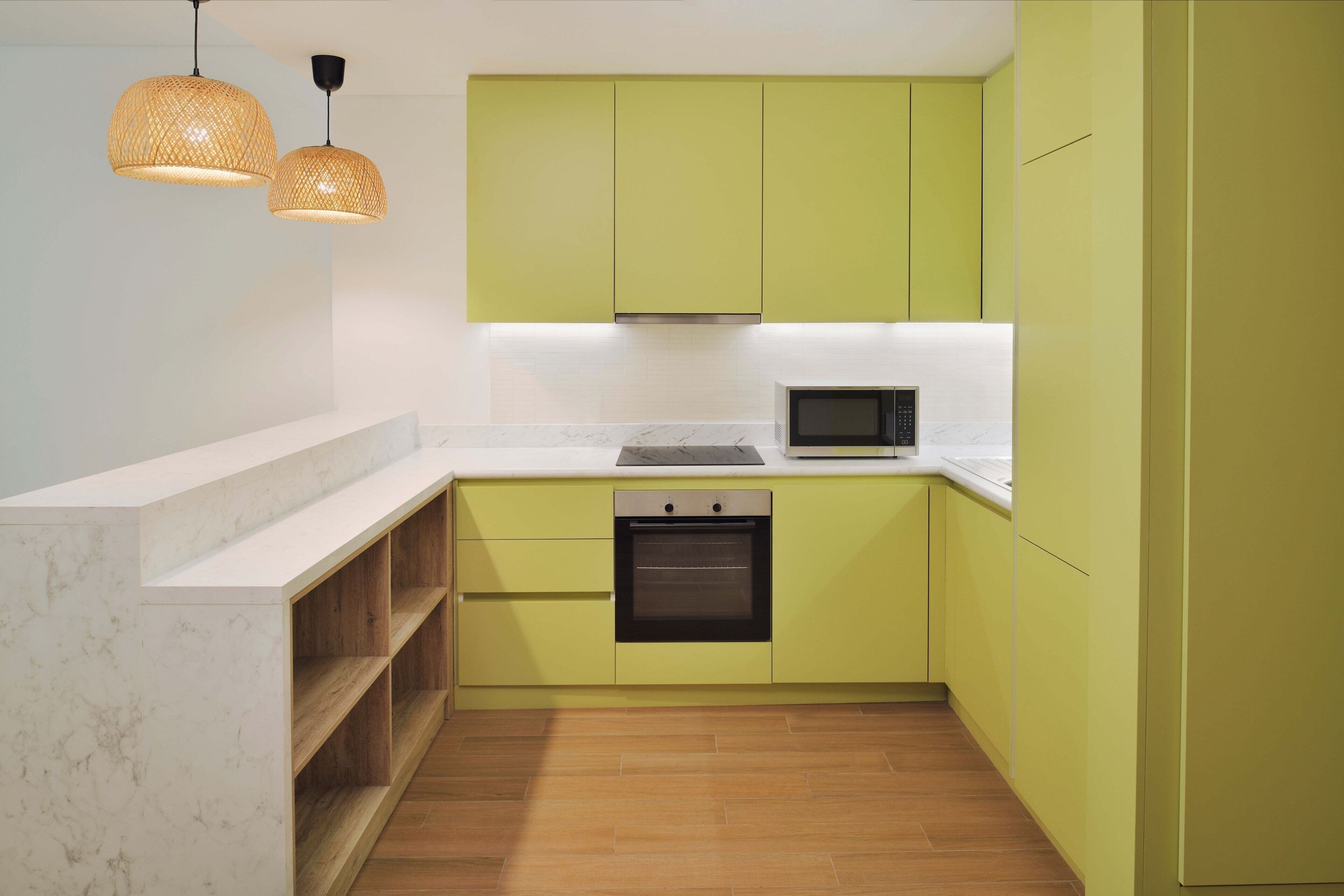 A compact kitchen with a built-in oven, a microwave, and a wooden shelf unit.