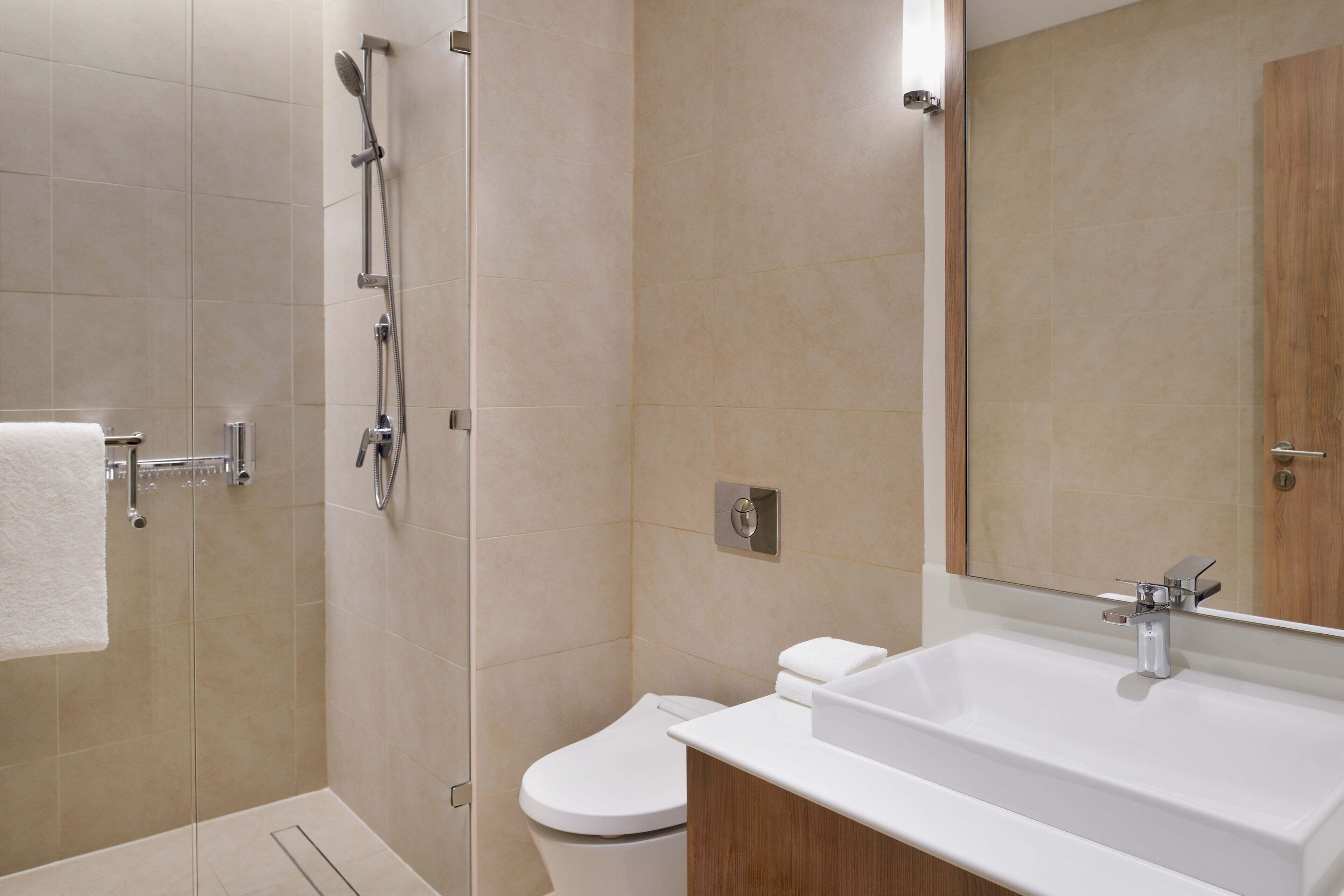 Un baño moderno con ducha envuelta en vidrio, inodoro blanco y un lavamanos grande con espejo arriba.