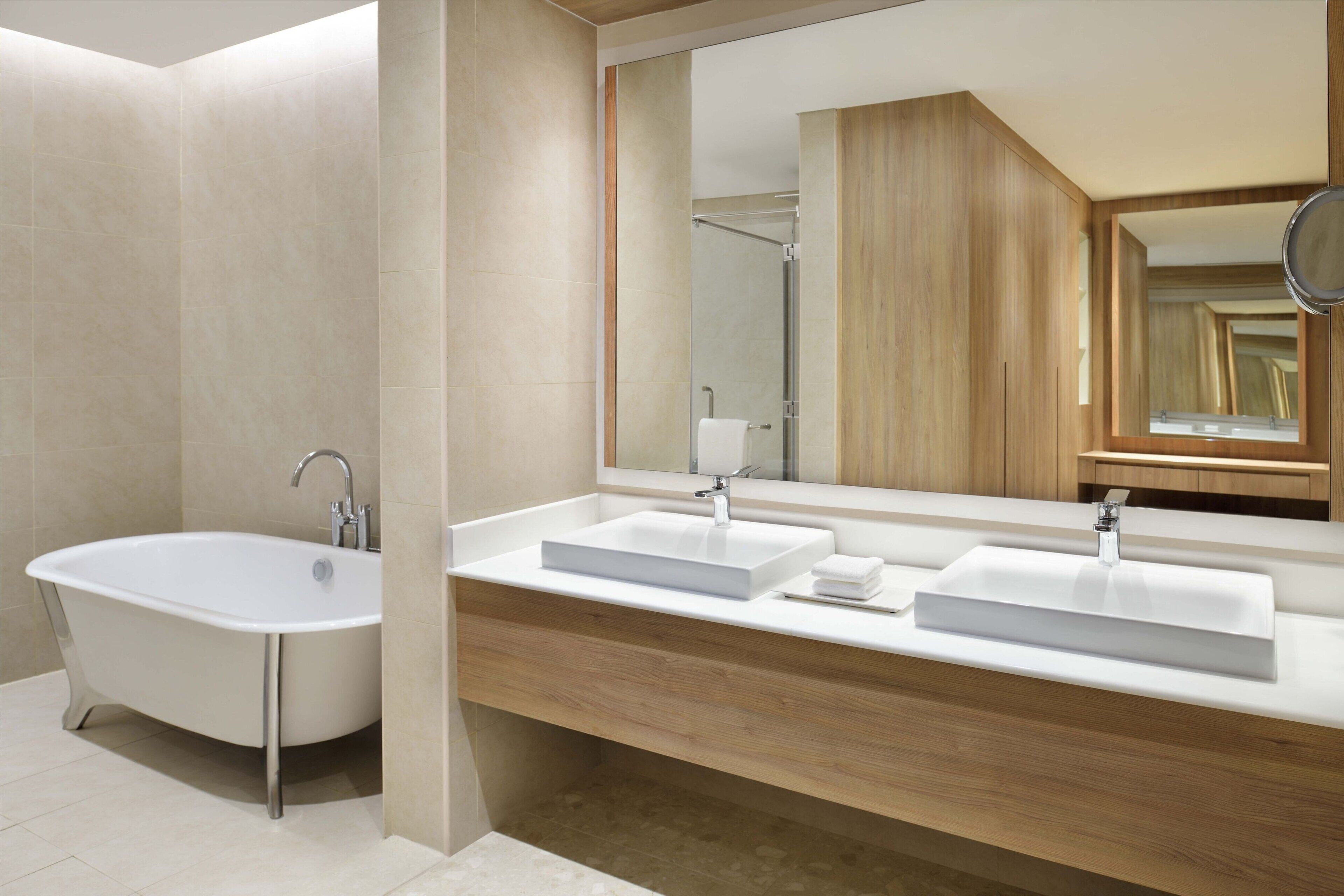 A modern bathroom with a freestanding bathtub, two sinks, and a large mirror.