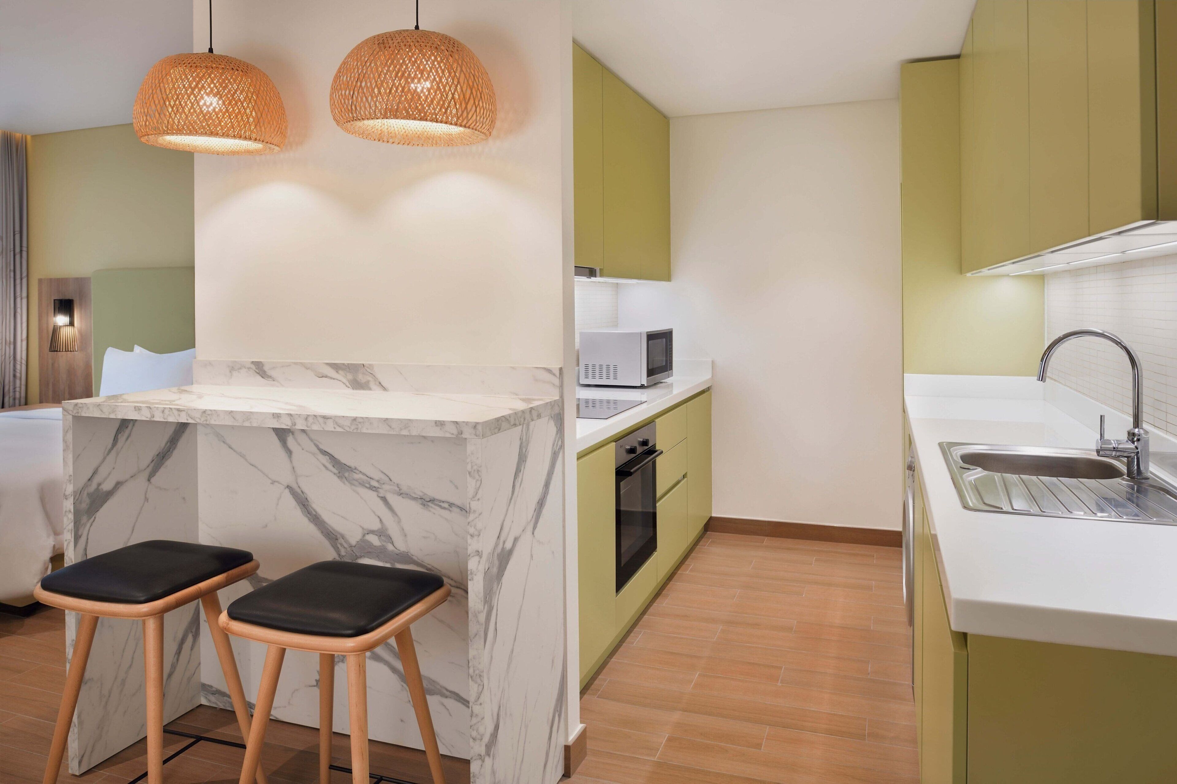 A modern kitchen with a marble island, green cabinets, a microwave, and two bar stools.