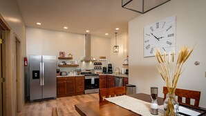 Une cuisine moderne avec des meubles en bois, un réfrigérateur en acier inoxydable et un coin repas comprenant une table et des chaises en bois.