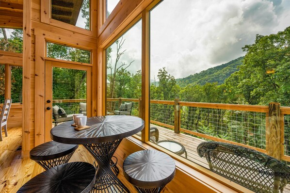 Una terraza de madera con una mesa y sillas, con vista a una ladera boscosa.