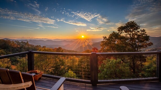 Une terrasse avec des chaises donnant sur un paysage montagneux au coucher du soleil.