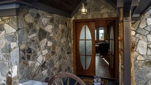 Un mur extérieur en pierre, une porte en bois avec des panneaux de verre dépoli et une chaise en bois.