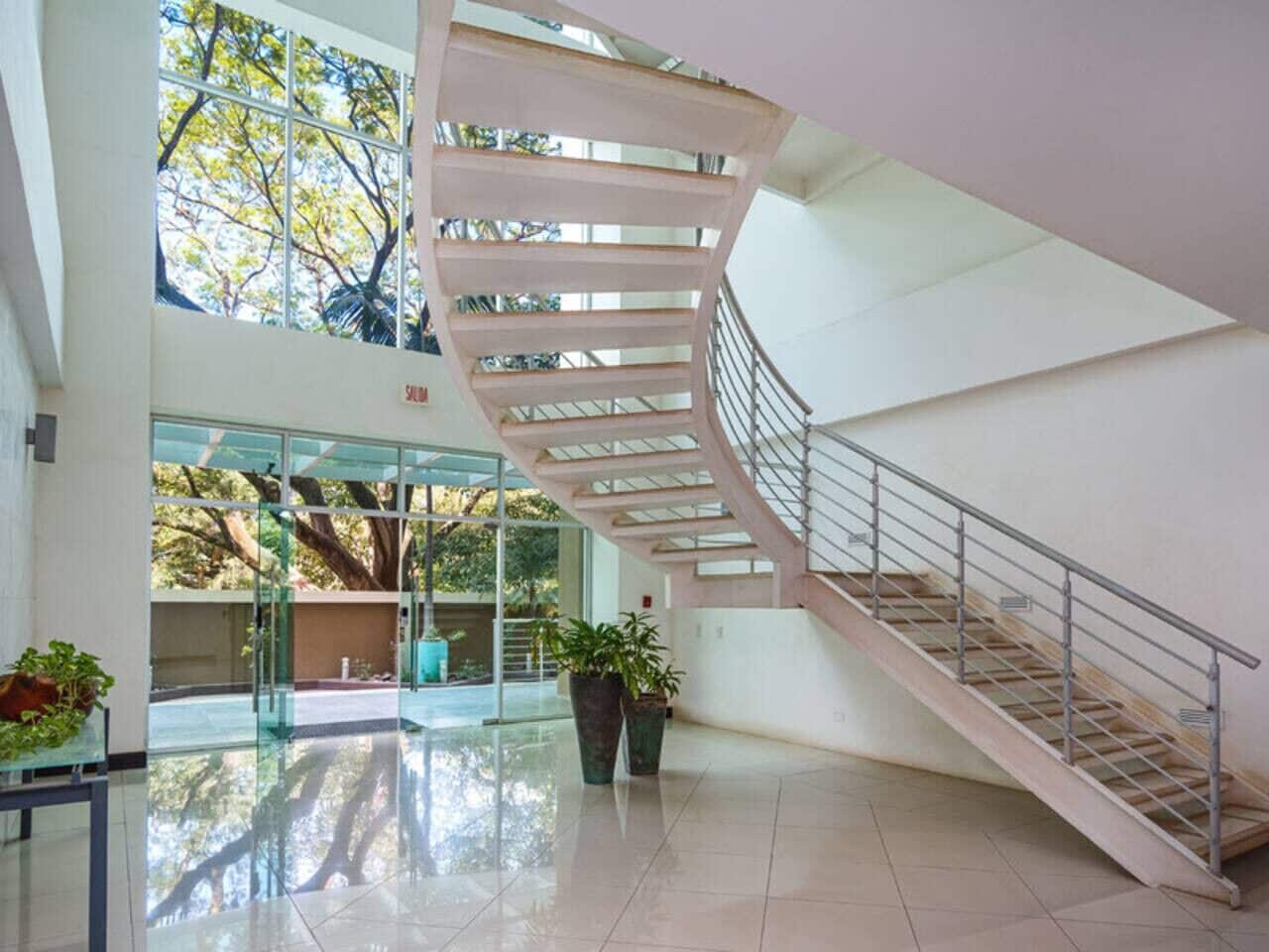 Un interior espacioso con una escalera de caracol, ventanas amplias y plantas en macetas.